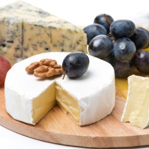 Assorted cheeses with grapes and walnut on wooden board.